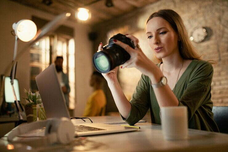 A girl is sitting in the office with a camera and checking the camera pictures.